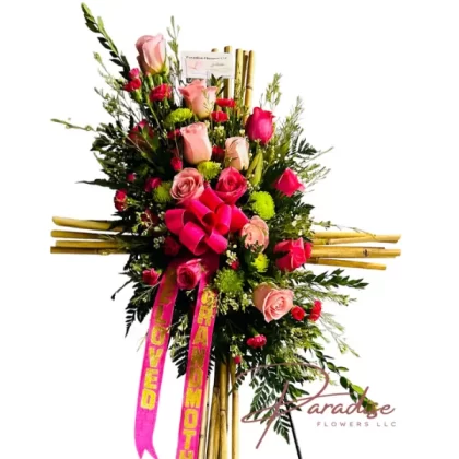 Bamboo Cross Sympathy Standing Spray with pink roses, mini carnations, green button pops, limonium, and bamboo, a tribute of love and remembrance.