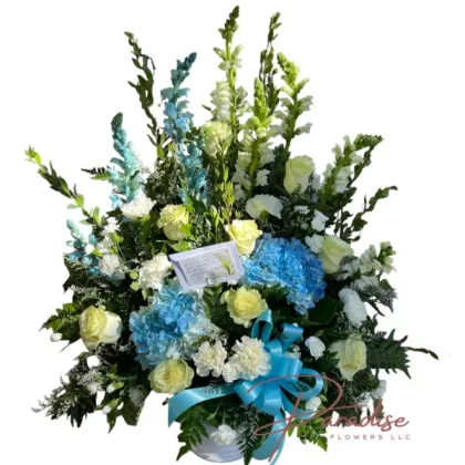 Blue and White Tribute floral arrangement featuring blue hydrangeas, white roses, snapdragons, limonium, and greenery.