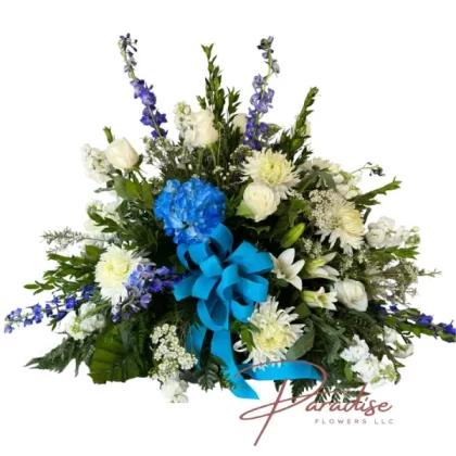 Blue Sky Casket Spray featuring white roses, lilies, spider mums, blue hydrangea, delphinium, and lush greenery.