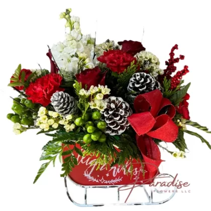 Christmas Day Sleigh holiday bouquet featuring white stock, red roses, red carnations, green hypericum, white waxflower, birch, white pine, and cedar in a vintage metal sleigh.