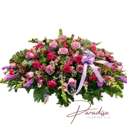 Garden of Grace Casket Spray featuring vibrant purples and pinks, with carnations, mini carnations, roses, snapdragons, delphinium, liatris, waxflowers, and greenery.