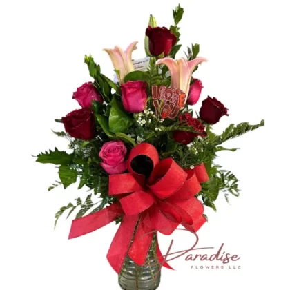 Love's Bloom Bouquet featuring red and pink roses, lilies, wax-flowers, and lush greenery.