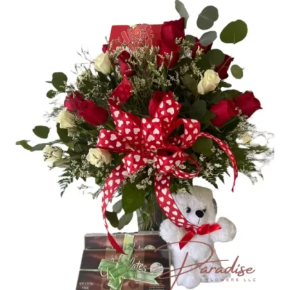 Three dozen red and white roses in a floral arrangement with a red heart ribbon, accompanied by chocolates and a plush teddy bear.