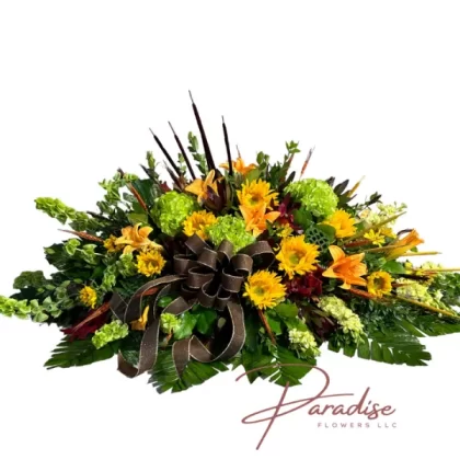 Sunshine Memories Casket Spray featuring sunflowers, orange lilies, green hydrangeas, yellow stocks, bells of Ireland, and lush greenery.