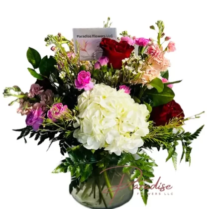 Sweet Arrival Bouquet featuring red roses, pink mini carnations, peach stocks, white hydrangeas, wax flowers, and green foliage.