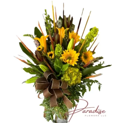 Vibrant Memories Tribute floral arrangement featuring white snapdragons, sunflowers, bells, orange lilies, green hydrangea, and safari flowers.