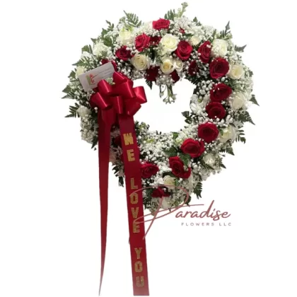 White and Red Heart of Love standing spray with red roses, white roses, and red and white spray roses in a heart-shaped design, accented by lush greenery.