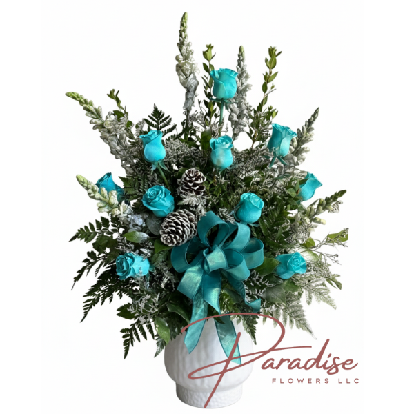 Winter Wonders Christmas arrangement featuring teal blue roses, silver snapdragons, frosted pine cones, and a teal bow in a white vase.