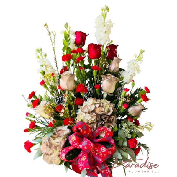 Festive Joy Arrangement Christmas centerpiece with red and gold roses, white stock, hydrangeas, and pine cones in a red ceramic vase.