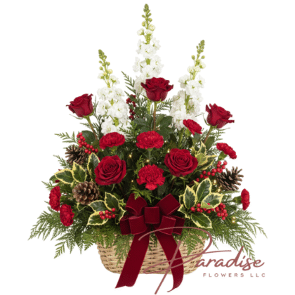 Rustic Christmas flower basket featuring red roses, white stock, red carnations, pinecones, variegated holly, and a red velvet bow.