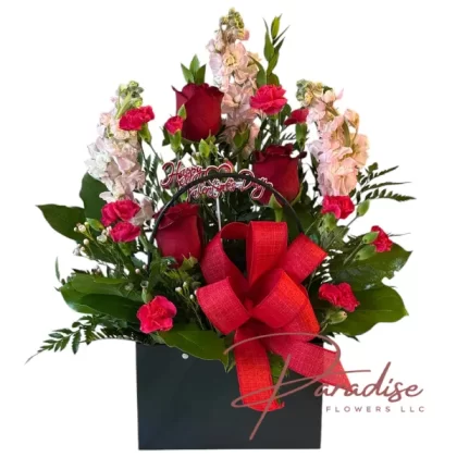 Blush of Love Handbag with pink stock, red roses, mini carnations, waxflowers, and greenery in a chic handbag container.