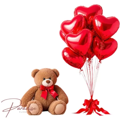 Large teddy bear with 12 red heart-shaped balloons and a red bow for Valentine’s Day.