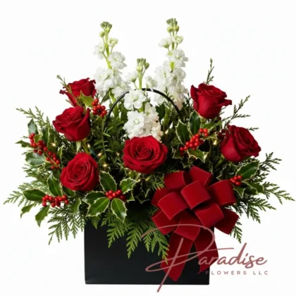 Modern Christmas flower arrangement with red roses, white stock, holly berries, and a red velvet bow in a sleek black box – Holiday gift idea by Paradise Flowers.