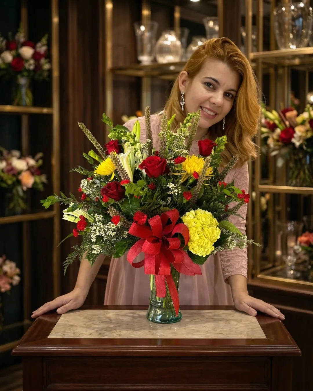 Portrait of Elizabeth Acosta, founder of Paradise Flowers LLC, standing proudly in her studio beside a large luxury arrangement of purple, white, and pink roses on a rustic wooden table.