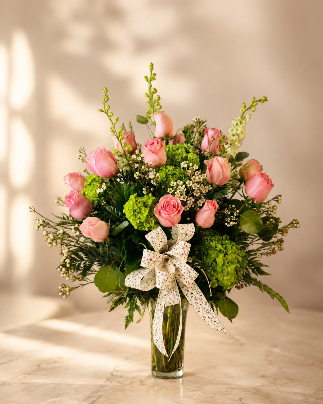 Pink roses and fresh greenery arranged in a glass vase by Paradise Flowers